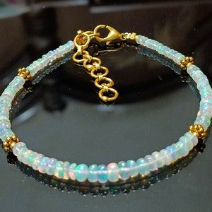 Puede incluir: Un delicado brazalete hecho con pequeñas cuentas de ópalo iridiscente y detalles dorados. El brazalete tiene un cierre dorado.