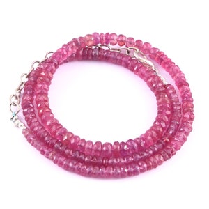 Puede incluir: Un collar de piedras preciosas rosas con un cierre de plata. El collar está hecho de pequeñas cuentas facetadas.