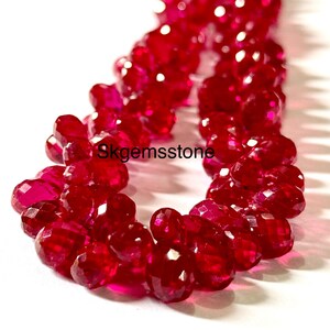 May include: Close-up of a strand of faceted, deep red gemstones. The gems are clustered together, reflecting light and creating a sparkling effect. The text "skgemsstone" is visible on the image.