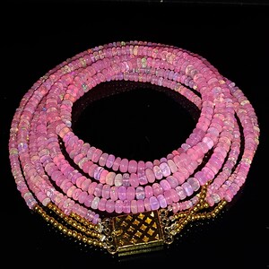 May include: A multi-strand necklace made of pink opal beads with a gold clasp. The necklace is layered and has a delicate, feminine look.