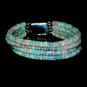 May include: A multi-strand bracelet composed of small, round, translucent opal beads. Each bead displays a play of color with flashes of green, orange, and pink. The bracelet is secured with a rectangular, polished silver-toned metal clasp.