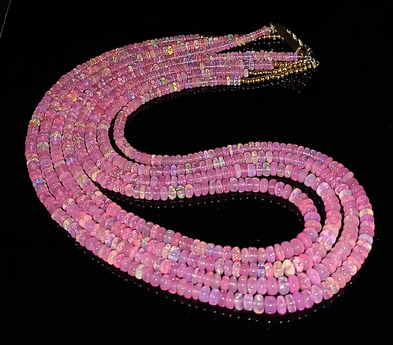 May include: A multi-strand necklace made of pink opal beads. The necklace is made of several strands of beads, and the beads are all a light pink color with a slight iridescent sheen.