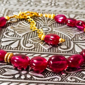 May include: A pink gemstone bracelet with gold accents. The bracelet is made of oval-shaped gemstones and gold beads.