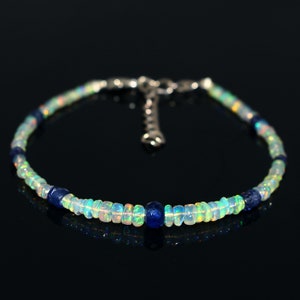 May include: A delicate bracelet made with iridescent white opal beads and dark blue sapphire beads. The bracelet has a silver clasp.
