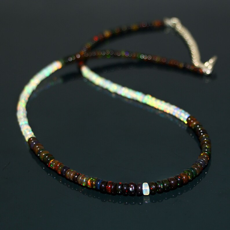 May include: A necklace made of small, iridescent opal beads in shades of brown, black, and white. The necklace is strung on a silver chain.