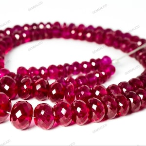 Puede incluir: Una hebra de cuentas de piedras preciosas de color rojo rubí, facetadas y redondas, enhebradas en un alambre de plata. Las cuentas están dispuestas en un patrón suelto y fluido.