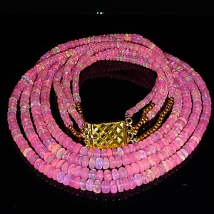 May include: A multi-strand necklace made of pink opal beads with a gold clasp.