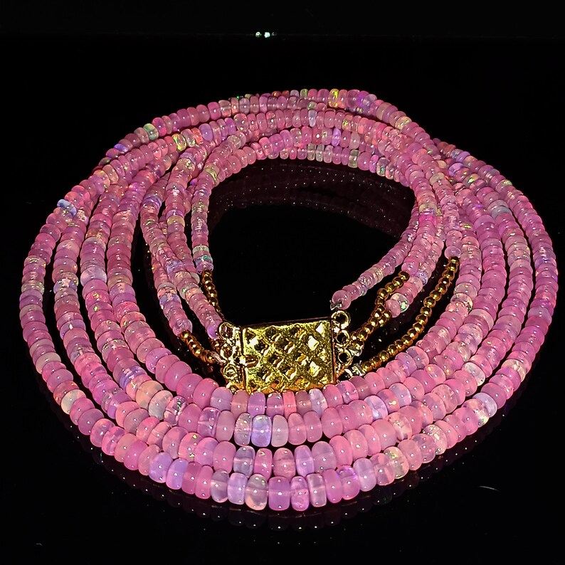May include: A multi-strand necklace made of pink opal beads with a gold clasp.
