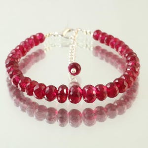 Puede incluir: Un brazalete de piedras preciosas rojas con cierre de plata y cadena ajustable. El brazalete está hecho de piedras preciosas rojas facetadas y tiene una longitud aproximada de 18 cm.