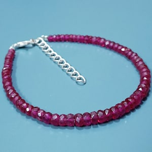 May include: A bracelet composed of small, faceted, deep pinkish-red gemstone beads arranged in a single strand. The piece features a silver-toned metal lobster claw clasp and an attached extender chain with oval links for adjustable sizing.