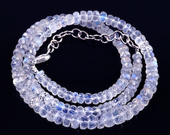 Op de afbeelding: Een delicate ketting bestaande uit meerdere strengen gefacetteerde, doorschijnende maansteen kralen. De kralen zijn zacht wit met subtiele blauwe en iriserende flitsen. De ketting is vastgezet met een zilverkleurige sluiting.