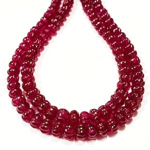 May include: A strand of deep red ruby beads, each bead is faceted and has a slightly rounded shape. The beads are strung together in a triple strand necklace.