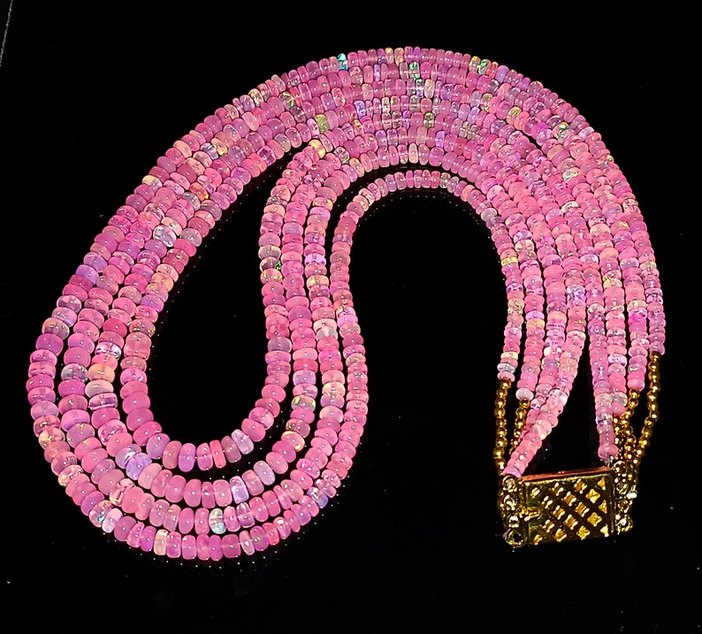 May include: A multi-strand necklace made of pink opal beads with a gold clasp.