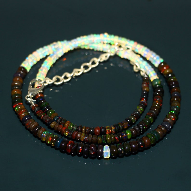 May include: A multi-strand necklace made of small, iridescent opal beads. The necklace is composed of two strands of dark, multi-coloured opal beads and one strand of white opal beads. The necklace has a silver clasp.