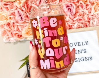 Puede incluir: Una lata de vidrio con un diseño rosa, naranja y amarillo que dice "Be Kind To Your Mind".