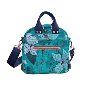 May include: A teal blue backpack with a floral print and a navy blue adjustable strap. The backpack has a zippered pocket and a top handle.