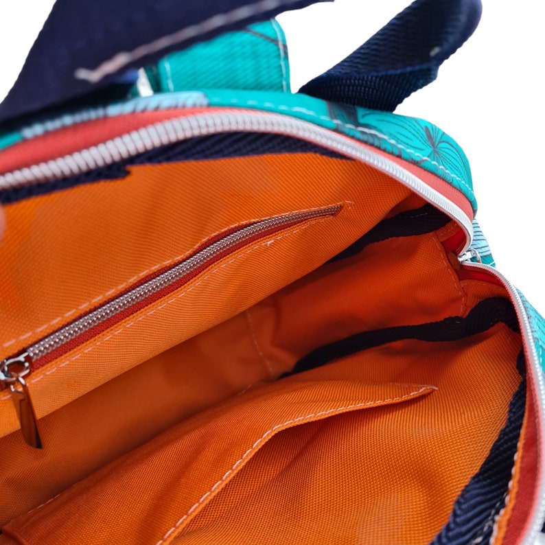 May include: The inside of a teal and orange backpack with a zippered pocket and an orange lining.