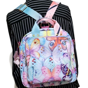 May include: A light blue and pink backpack with a butterfly print. The backpack has adjustable straps and a top handle.