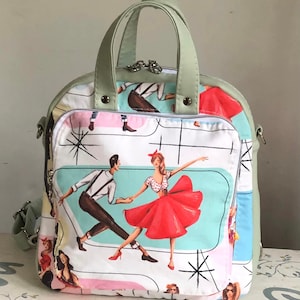 May include: A green and white patterned bag with a retro design featuring dancing couples. The bag has a top handle and a shoulder strap.