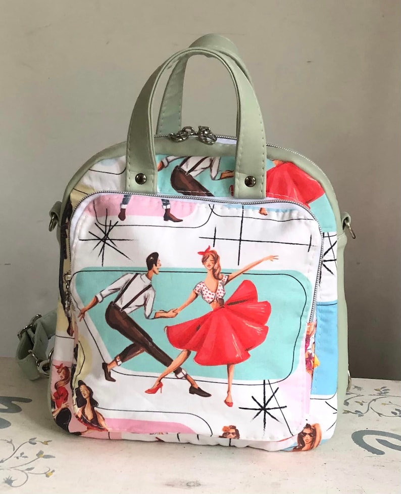 May include: A green and white patterned bag with a retro design featuring dancing couples. The bag has a top handle and a shoulder strap.