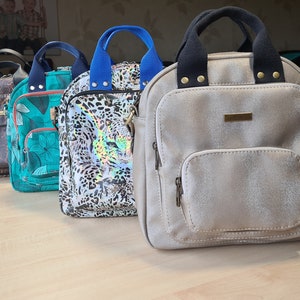 May include: Five different patterned backpacks with adjustable straps. The backpacks are in various colors, including white, brown, green, black, and beige.