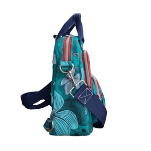 May include: A teal blue and green floral print crossbody bag with a navy blue strap and a silver clasp. The bag has a red zipper and a top handle.