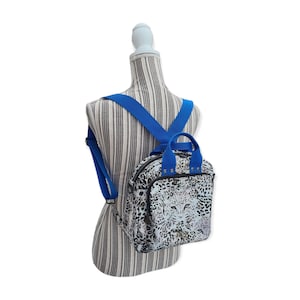 May include: A small, white and black leopard print backpack with blue straps. The backpack has a top handle and a zipper closure.