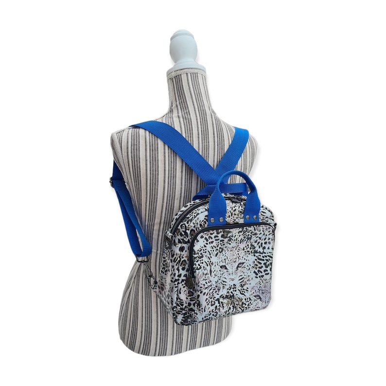 May include: A small, white and black leopard print backpack with blue straps. The backpack has a top handle and a zipper closure.