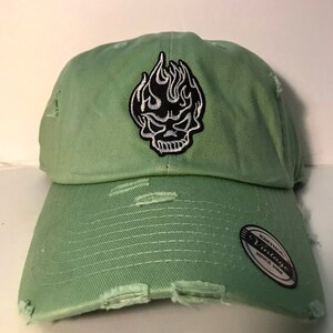 May include: A light green distressed baseball cap with a black and white skull and flame patch. The cap has a black and white "Vintage" label with the text "Koethnoy" and "Since 2008".