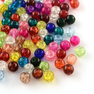 Könnte beinhalten: Eine Sammlung runder, mehrfarbiger Crackle-Glasperlen in verschiedenen Farbtönen wie Rot, Blau, Grün, Gelb, Pink und Transparent. Jede Perle weist eine ausgeprägte, innenliegende Bruchstruktur auf, die für ein reflektierendes Aussehen sorgt.