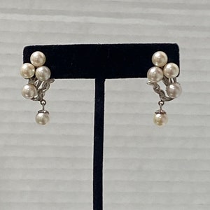May include: A pair of silver tone clip-on earrings with a cluster of faux pearls and a single pearl drop.