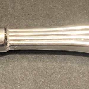 May include: A silver-colored, decorative bottle opener with a fluted handle and a clear, glass section at the end.