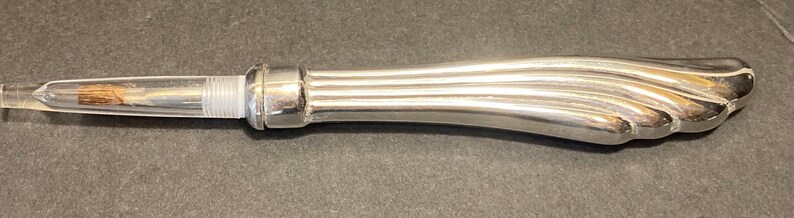 May include: A silver-colored, decorative bottle opener with a fluted handle and a clear, glass section at the end.