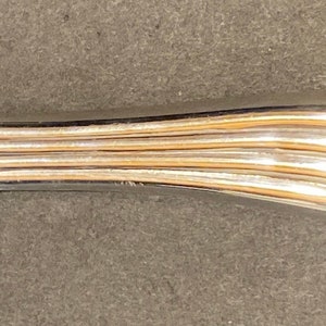May include: A silver makeup brush with a brown bristle brush head. The handle is fluted and has a rounded end.