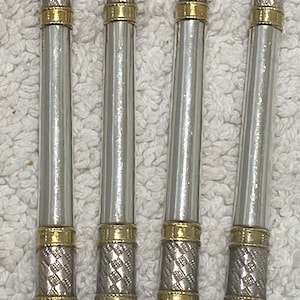 May include: Four silver-toned metal utensils with gold-colored accents. The handles have a textured design with gold bands at the top and bottom. The utensils are arranged vertically against a white background.