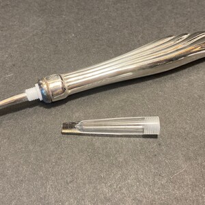 May include: A silver-toned brush with a long, fluted handle and a small, clear plastic tube. The brush has a small, brown bristle head.