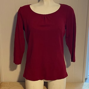 May include: A maroon long-sleeved shirt with a scoop neck and a gathered detail at the neckline.