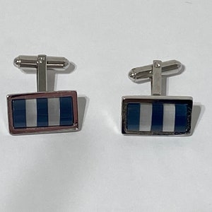 May include: A pair of silver cufflinks with a rectangular blue and white striped design.