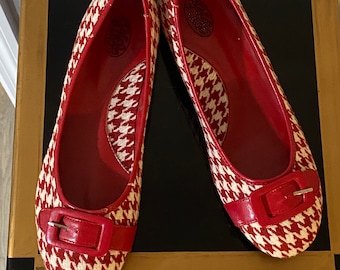 May include: A pair of red and white houndstooth flats with a red buckle. The flats have a pointed toe and a low heel.