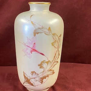 May include: A white ceramic vase with a gold rim and a floral design. The vase has a pearlescent finish and features pink and gold flowers.