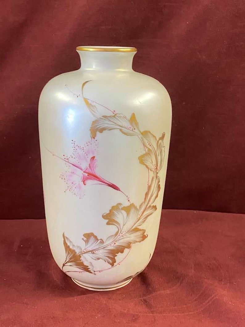 May include: A white ceramic vase with a gold rim and a floral design. The vase has a pearlescent finish and features pink and gold flowers.