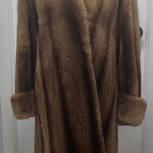May include: A long brown fur coat with a collar and cuffs. The coat is on a mannequin.