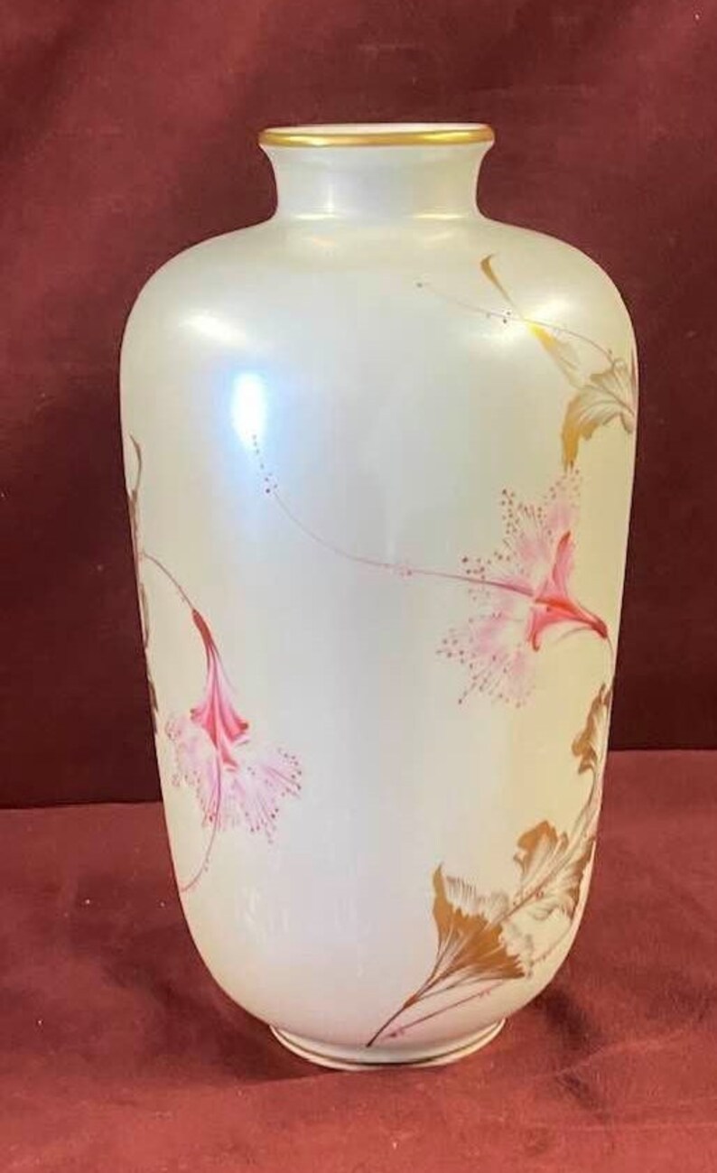 May include: A white ceramic vase with a gold rim and floral designs. The vase has a pearlescent finish and features pink and gold flowers.