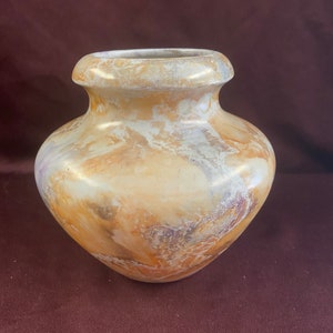May include: A small, round, ceramic vase with a marbled glaze in shades of cream, brown, and purple. The vase has a wide mouth and a rounded body.