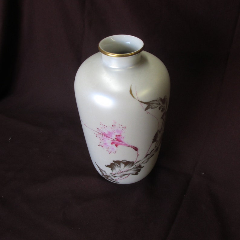 May include: A white ceramic vase with a gold rim and a pink floral design. The vase has a pearlescent finish.