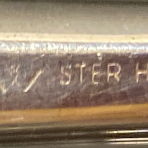 May include: Close-up of a silver-toned object with the inscription "STER H.H."