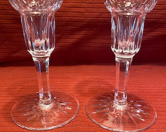 May include: Two clear glass candle holders with a cut glass design. The candle holders have a tall, slender stem and a wide base.
