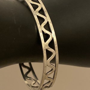 May include: A silver bangle bracelet with a wavy, cut-out design.