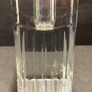 May include: A clear glass candle holder with a square base and a cylindrical opening for a candle. The holder has a textured, ribbed design.