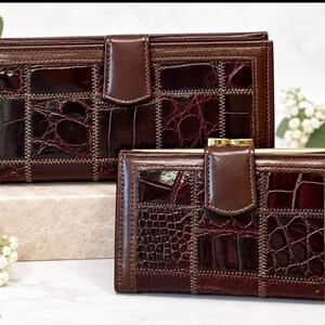 May include: Two brown wallets featuring a patchwork design with dark brown crocodile-embossed leather panels. The larger wallet has a snap-button closure, while the smaller wallet includes a gold-tone metal kiss-lock clasp and a snap-button tab.